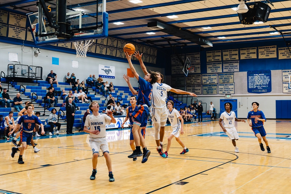 Basketball player doing a contested layup with player waiting for the rebound.
